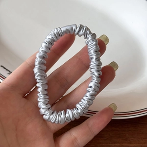 Close-up of a premium silver-grey silk satin hair scrunchie with elegant pleated texture