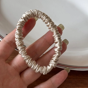 Close-up of champagne silk scrunchie showing detailed folds and smooth glossy texture