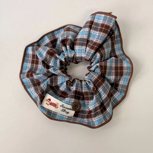 Detail of blue and brown plaid scrunchie with a brown button and Sweater Dog label