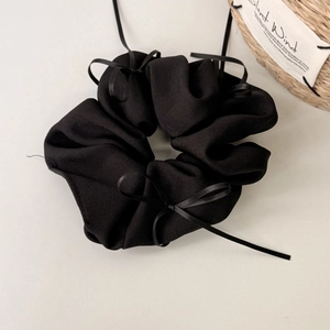 Détail d'un chouchou noir avec texture côtelée et petits nœuds sur un fond blanc épuré