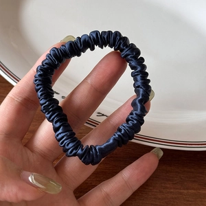 Detailed view of dark blue satin silk scrunchie with shiny pleated texture and high elasticity