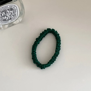Close-up of high-elastic dark green silk scrunchie with glossy pleated satin texture