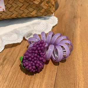 Gros plan d'un chouchou spirale violet avec pendentif raisin sur table en bois