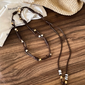 Bohemian dark brown braided waist chain with gold and white beads on wooden background