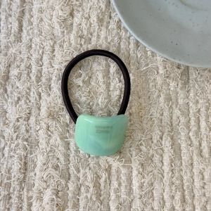 Detail of light green arc resin hair tie with France Handmade text on knit background