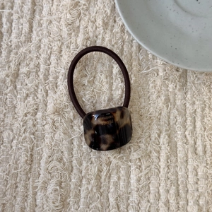 Detailed view of tortoise shell pattern hair tie with elastic brown cord on beige linen