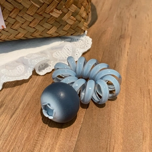 Gros plan d'un élastique spirale bleu avec une breloque myrtille mate sur bois