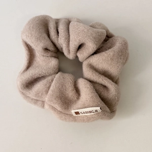 Close-up of beige plush scrunchie with soft lambskin texture and white brand label