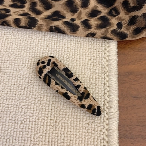 Detail of leopard print fabric hair clip on white knit background with retro aesthetic