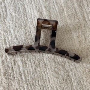 Detail view of leopard print hair claw clip with shell pattern on white fabric texture