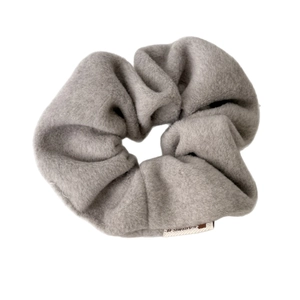 Plush grey fabric scrunchie with soft wool texture and white label on white background