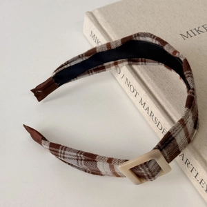 Detail of coffee and white plaid headband with a cream square buckle on a book
