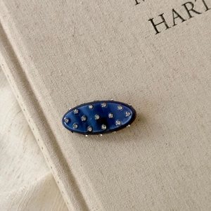 Vue macro d'une pince à cheveux ovale en résine bleu foncé ornée de seize strass brillants