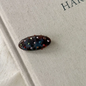 Détail macro d'une pince à cheveux ovale en acétate avec strass colorés sur un livre