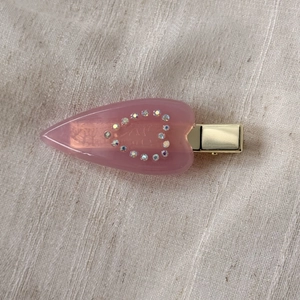 Detail of pink acetate hair clip showing sparkling rhinestone heart and golden metal grip
