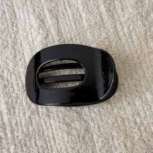 Detail view of a black glossy oval hollow hair claw clip with a sleek piano finish