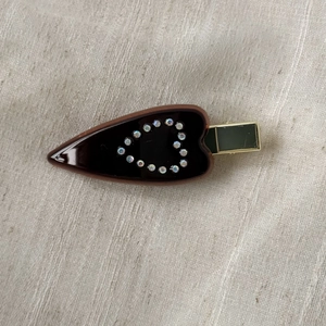 Detailed close-up of brown acetate hair clip with rhinestone heart on linen background