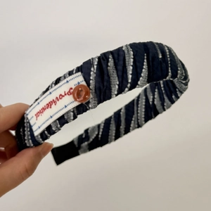 Dettaglio di un elastico per capelli a righe blu con etichetta rossa e bottone marrone