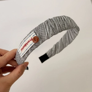 Dettaglio del cerchietto a pieghe grigio con etichetta Proidential e bottone decorativo