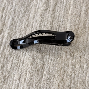 Detail of sleek black glossy hair claw clip with non-slip teeth on textured fabric