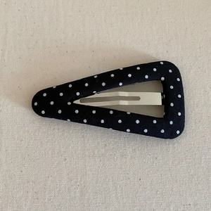 Detail view of a vintage black triangular BB clip with white polka dots on linen fabric