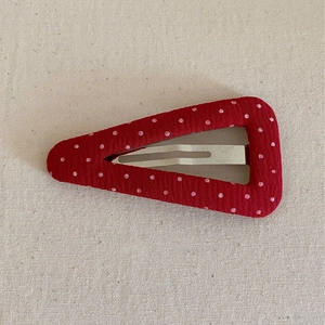 Detailed close-up of a red fabric hair clip with white polka dots and silver metal base