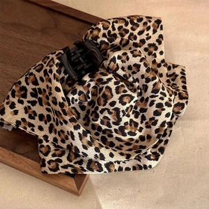 Elegant leopard print fabric claw clip on a dark wood tray with a beige background