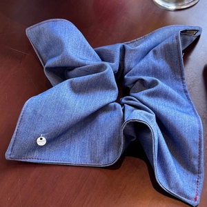 Macro shot of denim scrunchie with red stitching and silver brand charm on wood