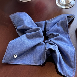 Detailed shot of a blue denim scrunchie with red stitching and a small metal logo plate