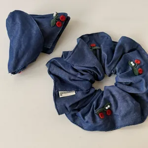 Detail of navy denim hair scrunchie with embroidered red cherries and Happiness label