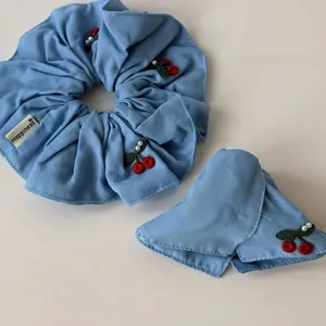Detail of light blue denim hair tie with red cherry embroidery and white pearls