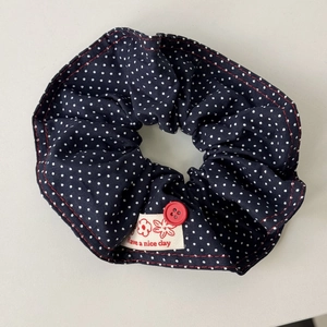 Detail of navy polka dot fabric headband with red button and woven quote label