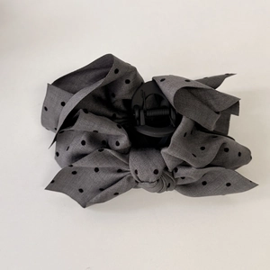 Detail of grey polka dot satin bow hair claw clip against a clean white background
