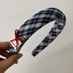 Detail of navy blue plaid headband featuring a red ribbon bow and handmade label