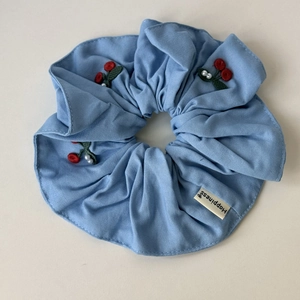 Detail of light blue denim hair scrunchie with cherry embroidery and Happiness label