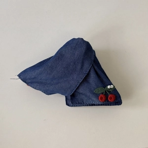 Detail of blue denim fabric with embroidered red cherries and white pearls on a hair clip