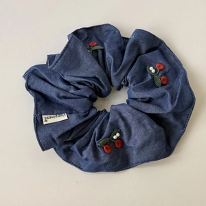 Detail of blue denim scrunchie with red cherry embroidery and elegant white pearl accent