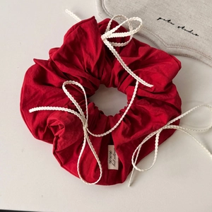 Close-up of red cotton scrunchie with white woven bow details and textured fabric