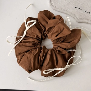 Detailed texture of brown cotton scrunchie featuring white woven rope and bow accents