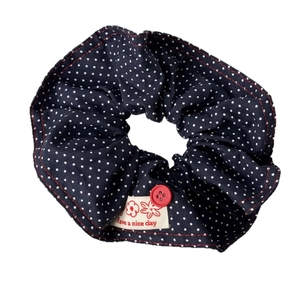 Navy blue polka dot hair scrunchie with red button and floral label on white background