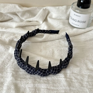 Dettaglio del cerchietto in tessuto scozzese antiscivolo con denti neri su lino bianco