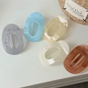 Cinq pinces à cheveux ovales en acrylique marbré disposées sur un bureau blanc épuré
