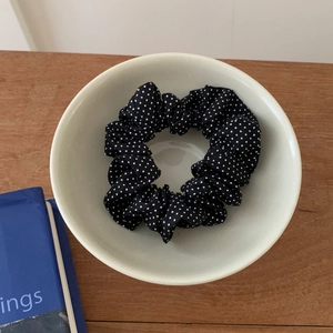 Detailed close-up of a black polka dot fabric scrunchie placed in a white ceramic bowl
