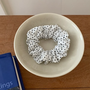 Detailed close-up of a white polka dot fabric scrunchie placed in a ceramic bowl
