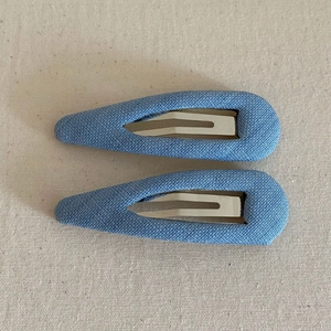 Detail of two light blue fabric-covered BB hair clips with silver metal inner snaps