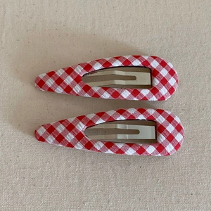 Close-up of two red and white gingham fabric-covered waterdrop BB hair clips on beige canvas