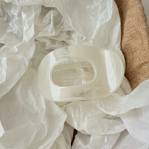 Détail de la pince à cheveux en acétate crème sur un tissu texturé neutre