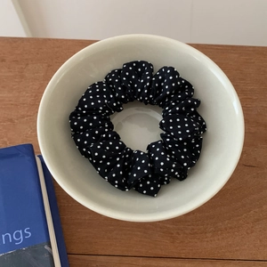 Detailed close-up of a black and white polka dot fabric scrunchie in a ceramic bowl
