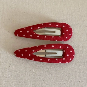 Detail of two red polka dot fabric BB hair clips on beige canvas texture background