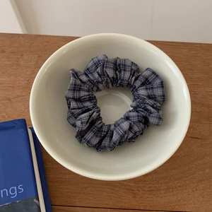 Detailed view of a blue and grey plaid fabric scrunchie with pleats in a ceramic bowl